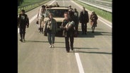 Filmszene aus "Im Zeichen des Kreuzes", Menschen laufen auf einer unbefahrenen Straße (Archivbild).  