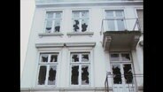 Eine Hausfassade mit zerschlagenen Fensterscheiben.  
