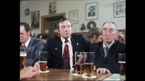 Mehrere Männer sitzen in einem Raum und trinken Bier  