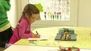 Ein Kind sitzt malend an einem Tisch.  