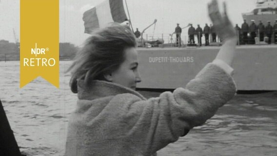 Frau winkt einem abfahrenden Marinekreuzer hinterher (1965)  