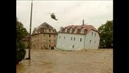 Ein über die Ufer getretener Fluss reißt ein Haus mit sich  