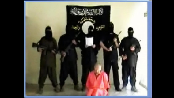 Eine Geisel kniet vor fünf schwarz gekleideten islamistischen Terroristen  