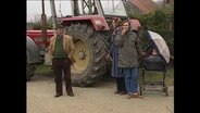 Drei Personen stehen vor einem Traktor  
