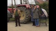 Drei Personen stehen vor einem Traktor  