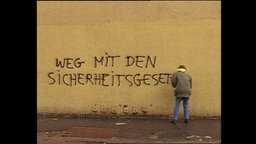 Ein Mann sprüht den Schriftzug "Weg mit den Sicherheitsgesetzen" an eine Mauer  