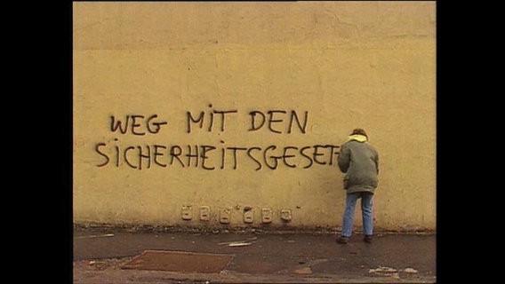Ein Mann sprüht den Schriftzug "Weg mit den Sicherheitsgesetzen" an eine Mauer  