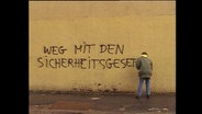 Ein Mann sprüht den Schriftzug "Weg mit den Sicherheitsgesetzen" an eine Mauer  
