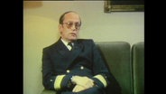 Admiralarzt Karl-W. Wedel sitzt auf einem Sofa  