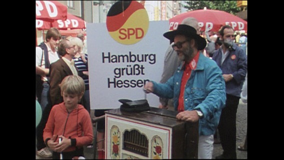 Ein Mann spielt einen Leierkasten, dahinter das Plakat" SPD Hamburg grüßt Hessen" (Archivbild)  