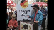 Ein Mann spielt einen Leierkasten, dahinter das Plakat" SPD Hamburg grüßt Hessen" (Archivbild)  