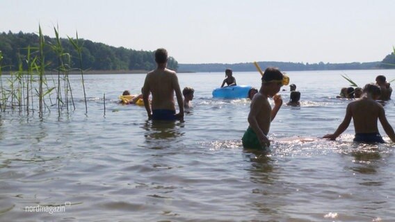 Kinder und Erwachsene baden in einem See.  