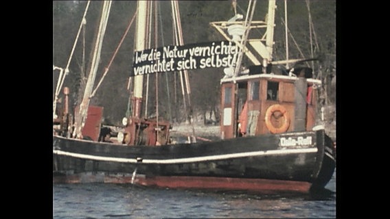 Ein Fischerboot mit einem Transperent für Umweltschutz zwischen den Masten  