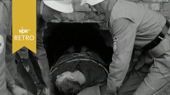 Katastrophenschützer ziehen bei einer Übung eine Bahre mit lebloser Person aus einem Kellerfenster (1963)  
