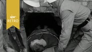 Katastrophenschützer ziehen bei einer Übung eine Bahre mit lebloser Person aus einem Kellerfenster (1963)  