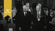 Göttinger Universitätsdirektor Arnold Scheibe und Professor Clark Kerr ziehen zu einer Festveranstaltung in einen Saal ein (1963)  