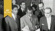 Mehrere Männer stehen um einen Togoer, der ein Buch ansieht (als Abschiedsgeschenk des Hamburger Senats 1964)  