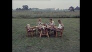 Eine Familie sitzt unter freiem Himmel am Esstisch  