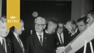 Mehrere ältere Herren, Teilnehmer einer Tagung über Raketentechnik, posieren neben dem Modell einer Rakete (1964  