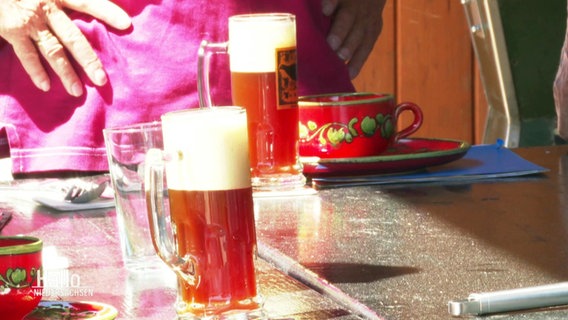 Blick auf zwei Biergläser, die gefüllt sind mit naturtrüben, bernsteinfarbenen Bier.  
