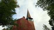 Ein Kirchturm vor bewölktem Himmel  