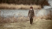 Eine Frau spaziert alleine am Ufer eines Flusses  