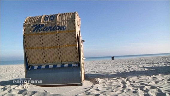 Ein Strandkorb steht am Strand vor strahlend blauem Himmel  