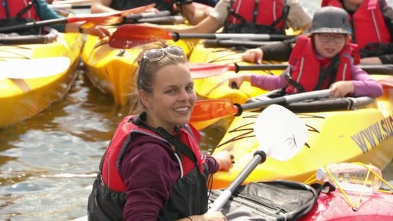 Eine Stadtführerin einer Kajak-Tour in Stralsund inmitten von anderen Kajaks im Wasser.  