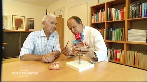Ein Arzt und ein Patient sitzen vor einem Herz-Modell  