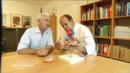 Ein Arzt und ein Patient sitzen vor einem Herz-Modell  