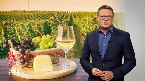 Bertil Starke mit einem Symbolbild mit Weinbergen und einem Brettchen mit Weintrauben, Käse und einem Glas Weißwein.  