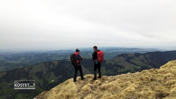 Zwei Männer mit Wanderrucksäcken stehen auf einem Berg  