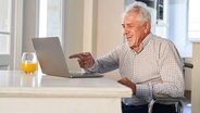 Ein älterer Herr lachend vor dem Laptop.  