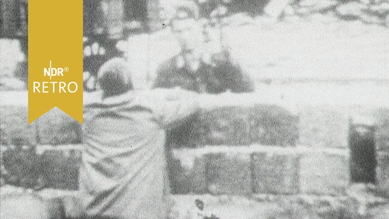 Ein Zivilist und ein Grenzer unterhalten sich beim Mauerbau über diese hinweg (1963)  
