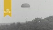 Fallschirmspringer über einem Waldstück im Flug (1963)  