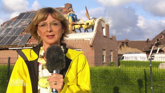 Reporterin Gerlach vor Ort, im Hintergrund ein zerstörtes Haus.  