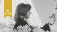 Junge Frau hält vor einer Schiffstaufe die Sektflasche in der Hand und lächelt (1964)  