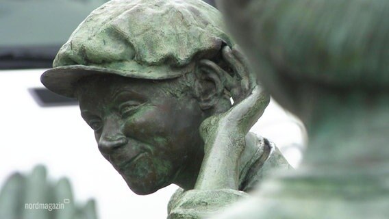 Nahaufnahme von einer Statue in Hagenow. Ein Junge mit einer Schiebermütze hält sich seine Hand hinter sein Ohr als wolle er besser hören, dabei grinst er.  