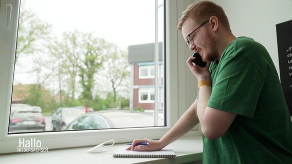 Ein Mann steht an einem Fenster und telefoniert.  