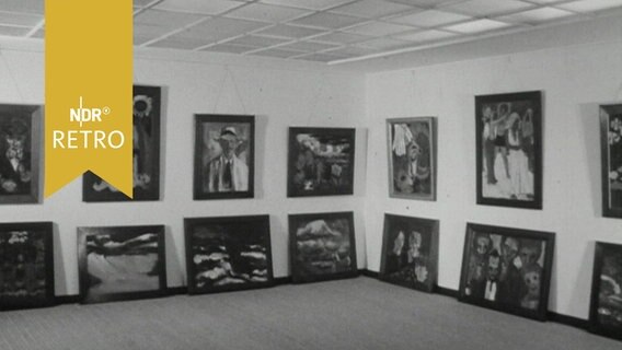 Ausstellungsraum im Emil-Nolde Museum Niebüll 1964: Bilder hängen an den Wänden, darunter stehen Bilder auf dem Fußboden  