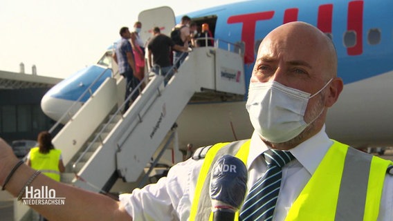 Ein Mann mit Maske - Pilot Oliver Fischer - steht auf einem Rollfeld vor einer Maschine von TUIfly.  