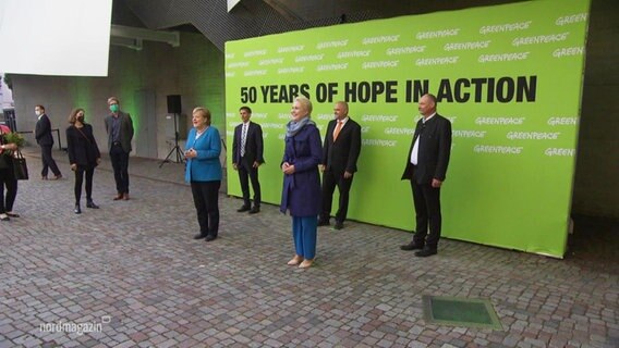 Angela Merkel steht vor einem Greenpeace Plakat.  