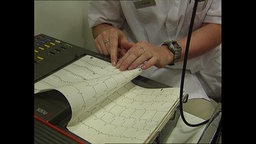Eine Ärztin mit Stethoskop blickt auf EEG Ergebnisse  
