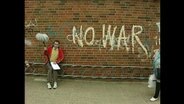 Alfons neben einem Graffiti gegn Krieg  