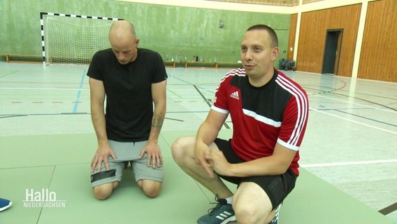 Sebastian Pargmann (rechts im Bild) im Interview. Er und weitere Auszubildende trainieren in einer Turnhalle.  