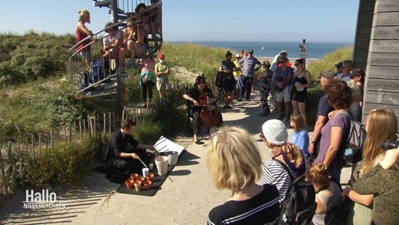 Menschen haben sich um zwei Musiker versammelt, die am Wegesrand mitten in den Dünen von Norderney ihre Instrumente spielen.  