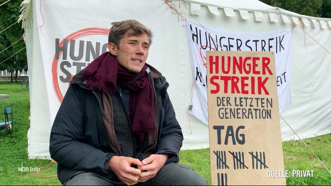 Ein junger Mann sitzt neben einem Plakat mit der Aufschrift: Hungerstreik der letzten Generation.