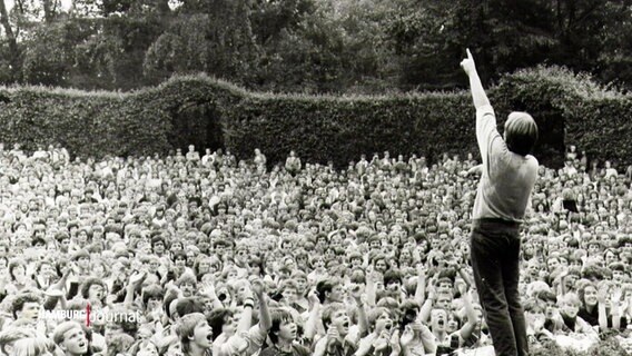 Schwarz-Weiß-Bild: Herbert Grönemeyer (von hinten zu sehen) steht auf der Bühne des Hamburger Stadtparks und reckt den Arm in die Luft  