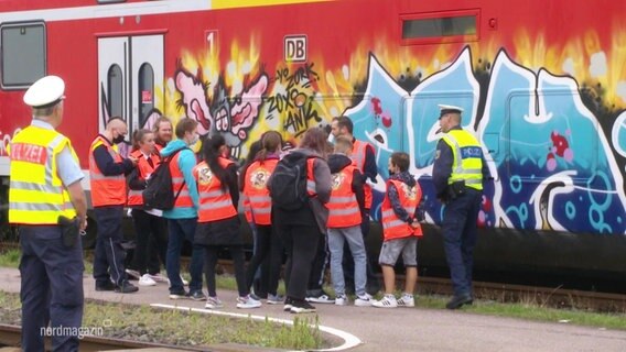Schülerinnen und Polizistinnen vor einem Zug mit Graffitibemalung.  