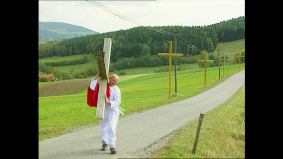 Ein Mann mit Kreuz auf der Schulter geht die Straße entlang  